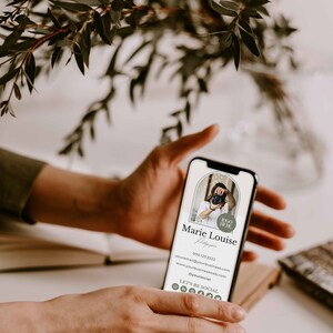 May include: A mobile phone displaying a digital business card for a photographer named Marie Louise. The card includes her name, phone number, email address, website, and social media links. The card has a minimalist design with a neutral color palette.