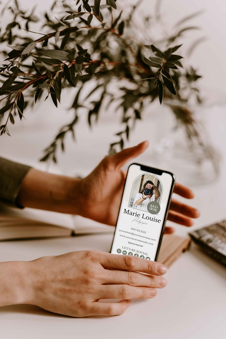 May include: A mobile phone displaying a digital business card for a photographer named Marie Louise. The card includes her name, phone number, email address, website, and social media links. The card has a minimalist design with a neutral color palette.