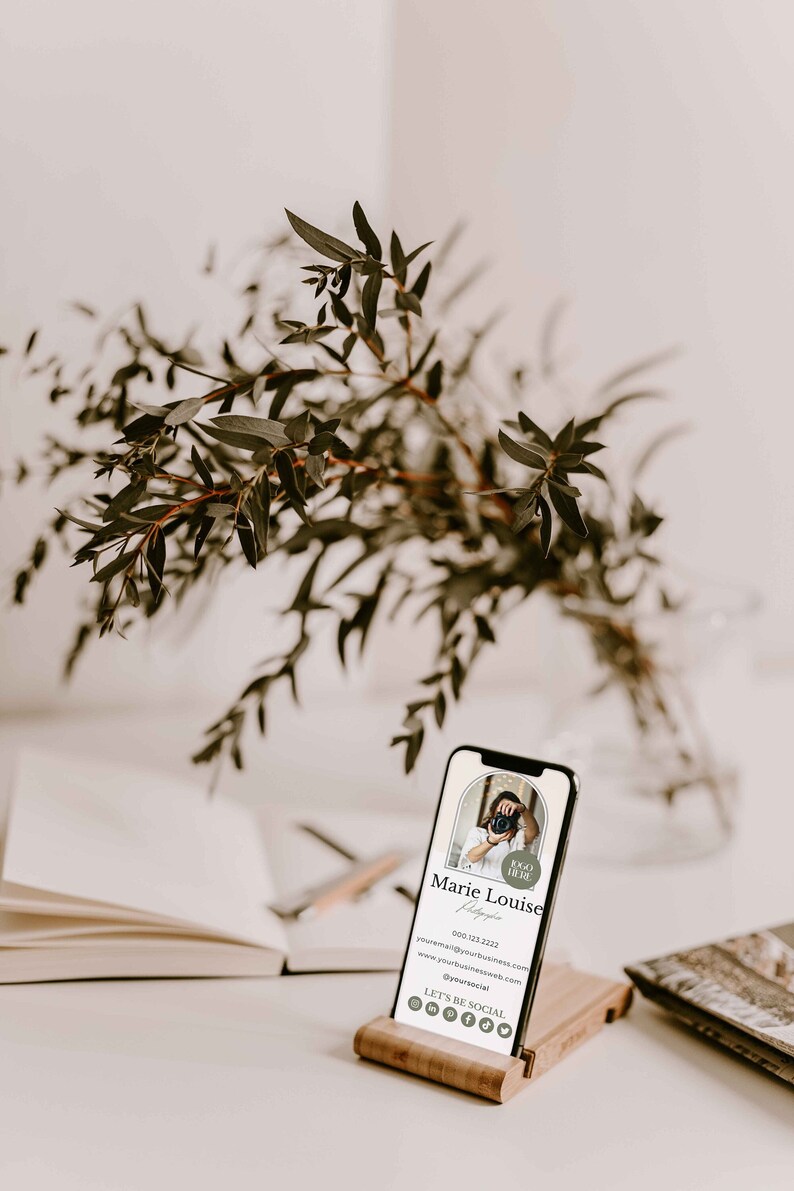 May include: A digital business card on a wooden stand. The card features a photo of a person holding a camera, the text "Marie Louise Photography", a phone number, email address, website address, social media icons, and the text "Let's be social".