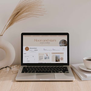 K&ouml;nnte beinhalten: Ein Laptop-Computer zeigt eine Website f&uuml;r einen Shop namens "Moon and Stars" mit dem Slogan "magic making". Die Website verf&uuml;gt &uuml;ber eine Suchleiste, ein Kategoriemen&uuml; und ein Raster mit Produktbildern. Der Laptop steht auf einem Holztisch mit einer Tasse Kaffee und einem Stapel B&uuml;chern.