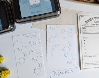 May include: An assortment of stationery supplies, including ink pads, stamps, and printed cards. The ink pads are in black and light blue, with Japanese text. The cards feature blue bubble designs and the text "Light Blue" and "Masuhana".