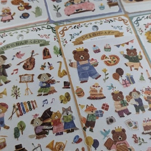 May include: Two sheets of stickers featuring adorable animal illustrations. The first sheet features a band of animals playing musical instruments, including a dog playing the violin, a cat playing the piano, and a wolf playing the cello. The second sheet features a group of animals celebrating a birthday, including a bear wearing a crown and holding a cake, a fox carrying a present, and a dog holding a balloon.