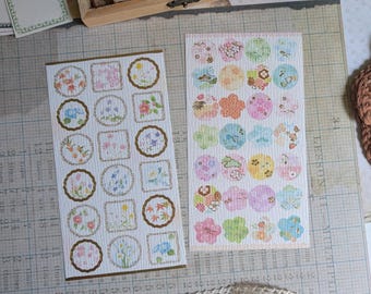 May include: Two sheets of decorative stickers featuring floral and circular designs. One sheet has square and circular frames with flowers. The other sheet has colorful circles with floral and animal patterns. A lace ribbon and wooden stamps are also visible.