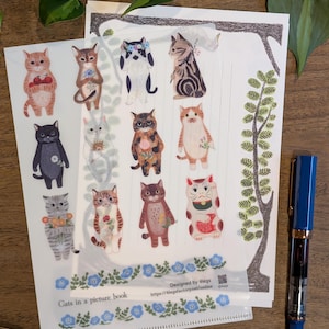 May include: Sheets of cat-themed stickers with various cat illustrations, some holding flowers or wearing accessories. The stickers are on white paper with a blue floral border and the text "Cats in a picture book". A blue pen is on the right.