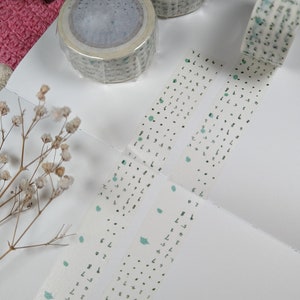 May include: Three rolls of washi tape with a white background and green and black patterns. The tape features a repeating pattern of small green dots, larger green dots, and black handwritten numbers.