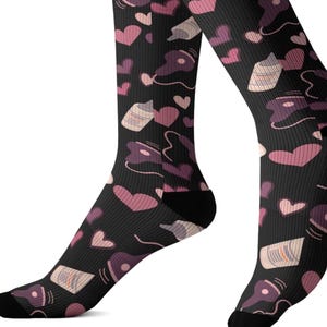 Può includere: Calzini neri con un motivo ripetuto di cuori rosa, flaconi di profumo e note musicali. I calzini sono al ginocchio e hanno talloni e punte neri.