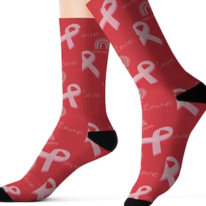 Könnte beinhalten: Ein Paar rote Socken mit einem rosa Schleifenmuster und dem Wort "love", das sich wiederholt. Die Socken haben auch eine kleine Regenbogengrafik.