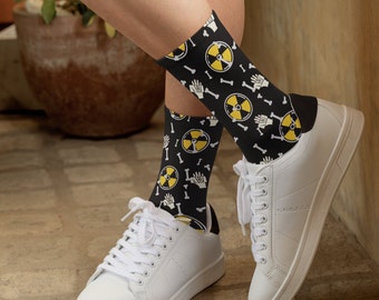 May include: A pair of black socks with a yellow and black pattern of radiation symbols and bones. The socks are being worn with white sneakers.