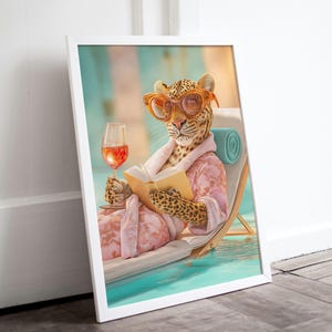 Könnte beinhalten: Gerahmter Kunstdruck, der einen Leoparden mit Sonnenbrille und rosa Bademantel zeigt, der sich auf einem Poolstuhl entspannt, ein Buch liest und ein Weinglas hält. Der Leopard befindet sich in einem Pool mit blau-weißem Hintergrund.