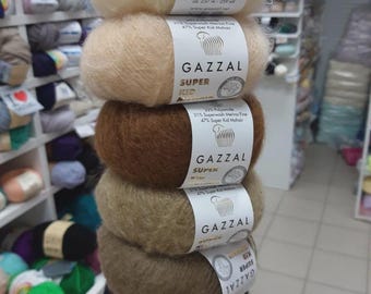 May include: A stack of Gazal Super Kid Mohair yarn balls in various colors, including cream, tan, brown, and black. Each ball is labeled with the brand name and fiber content. The yarn is 25g or 0.88 oz.