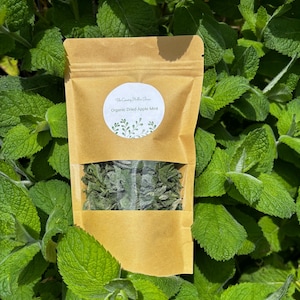 May include: A brown paper pouch with a clear plastic window containing dried green leaves. A white circular label on the front features the text The Country Hollow Farm and Organic Dried Apple Mint with a small green leaf illustration.