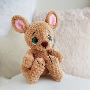 May include: A handmade, plush toy mouse in shades of brown. The mouse has large, expressive eyes with green irises, a brown nose, and pink-lined ears. Its paws are detailed with stitched claws. The toy is made of a soft, textured material.