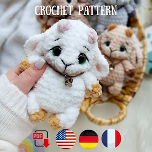 Puede incluir: Un cordero de ganchillo blanco con ojos verdes, un collar marrón y una pequeña campana. El cordero se sostiene en una mano. La imagen incluye el texto "CROCHET PATTERN" y banderas de EE. UU., Alemania y Francia.