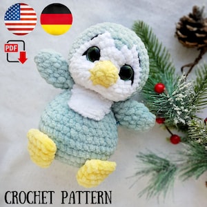 May include: Crochet pattern for a blue penguin amigurumi toy with yellow feet and a white belly. The penguin is sitting on a white surface with a pine branch and red berries in the background.