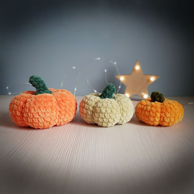 May include: Three crocheted pumpkins in orange, cream, and orange. The pumpkins are made with yarn and have a fuzzy texture.