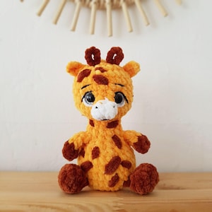 May include: A crocheted giraffe plush toy with brown spots and large eyes. The giraffe is sitting on a wooden surface.
