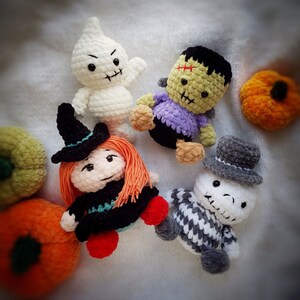 May include: A set of five crocheted Halloween-themed toys. The toys include a ghost, a witch, a zombie, a skeleton, and a pumpkin. The toys are all made with different colored yarn and have different facial expressions.