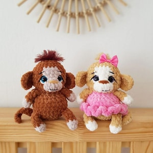 May include: Two crocheted monkey plushies, one brown with a brown tail and the other tan with a pink dress and a pink bow.