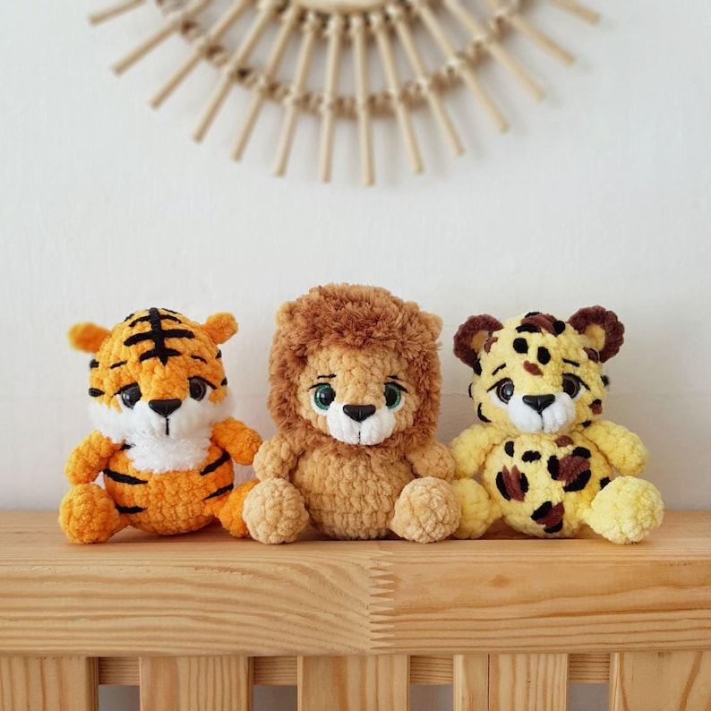 May include: Three crocheted stuffed animals: a tiger with orange and black stripes, a lion with brown fur, and a cheetah with yellow fur and brown spots.