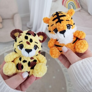 May include: Two crocheted stuffed animals, a tiger and a leopard, both with yellow fur and black stripes or spots. The tiger has white fur on its chest and a black nose. The leopard has brown spots.