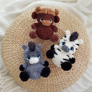 May include: Three crocheted stuffed animals: a brown bull, a gray donkey, and a black and white zebra. The animals are sitting on a woven brown basket.