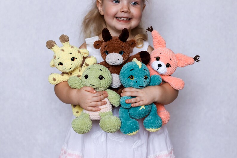 May include: A young child is holding a collection of crocheted stuffed toys. The toys include a giraffe, a bull, a dinosaur, and a squirrel. The toys are all made with soft, colourful yarn.