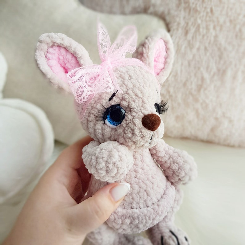 May include: A handmade plush mouse in soft grey with pink inner ears and a pink lace bow. The mouse has blue eyes, long eyelashes, and a brown nose. The toy is a cute, cuddly design.
