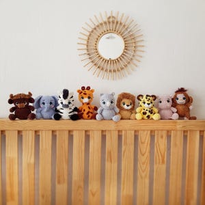 May include: A collection of eight crocheted animal toys, including a zebra, giraffe, elephant, lion, rhino, monkey, cheetah, and bull, arranged on a wooden shelf.