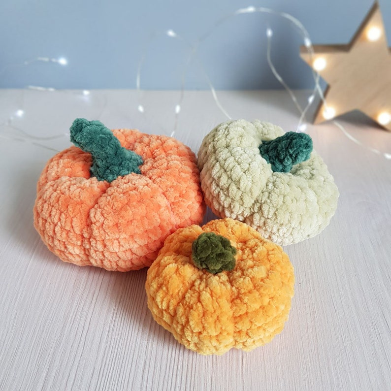 May include: Three crocheted pumpkins in orange, yellow, and green. The pumpkins are made of yarn and have a fuzzy texture.