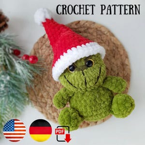 Könnte beinhalten: Häkelanleitung für eine grüne Grinch-ähnliche Kreatur, die einen roten und weißen Weihnachtsmann-Hut trägt. Das Muster ist im PDF-Format erhältlich und enthält Anleitungen in Englisch und Deutsch.