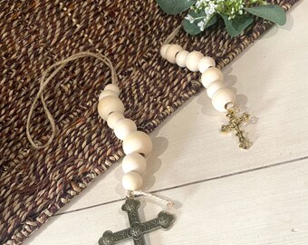 May include: Two wooden bead garlands with gold cross charms. The garlands are hanging from a woven basket.