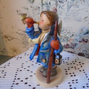 May include: A porcelain figurine of a boy in a blue coat and red mittens blowing a horn. He is holding a staff with a lantern attached. The figurine is standing on a round base.