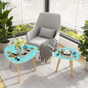 May include: Two turquoise, mid-century modern style side tables with a cat and book design. The tables have light wood legs and a rounded triangular shape. One table has a vase of flowers, the other has a coffee cup.
