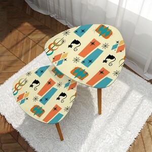 May include: Two retro-style side tables with a cream-colored surface. The tables feature a repeating pattern of black cat silhouettes, orange and blue rectangles, diamonds, and starbursts. The tables have three wooden legs.