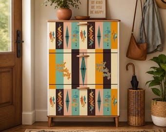 May include: A wooden chest of drawers with three horizontal drawers featuring mid-century modern geometric patterns in teal, orange, brown, and cream. The middle drawer displays the text "good vibes only" in a cursive script on both sides.