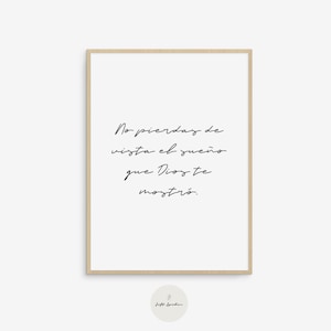 May include: A framed print with the text "No pierdas de vista el sueño que Dios te mostró" in elegant cursive script. The print has a white background and a light brown wooden frame. A small circular logo is at the bottom.