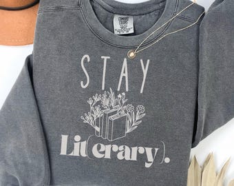 May include: A gray sweatshirt with the text "STAY literary." in white. The text is surrounded by a graphic of books and flowers.