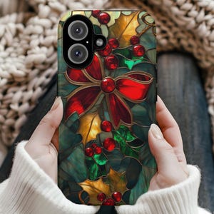 May include: A smartphone case featuring a stained-glass design with a red bow, holly leaves, and red berries. The case has a dark green background with gold and green accents, creating a festive holiday theme.