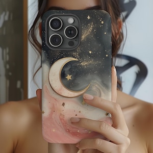 Puede incluir: Una funda de teléfono negra con un diseño de mármol rosa y dorado y una luna creciente dorada con una estrella. La funda tiene una cubierta de lente de cámara negra.