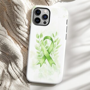 May include: A white phone case with a green ribbon and leaves design. The ribbon is a symbol of support and awareness for various causes.