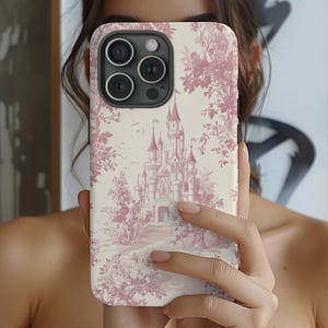 May include: A pink and white phone case with a floral pattern and a picture of a castle. The case is designed for an iPhone with a triple lens camera.