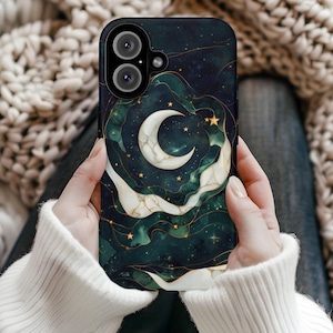 May include: A phone case featuring a celestial design with a crescent moon, stars, and swirling clouds in shades of green, white, and gold. The case has a dark background and a glossy finish. The phone case is held by a person wearing a white sweater.