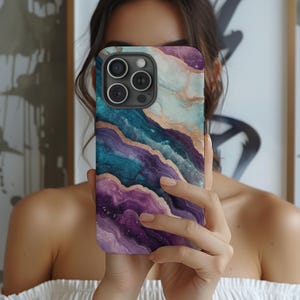 May include: A phone case with a colorful abstract design featuring swirls of teal, purple, and gold. The case has a raised camera bump with three lenses.