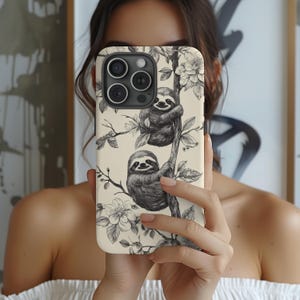 May include: A white iPhone case with a black and white illustration of two sloths hanging from branches with flowers. The case has a camera lens cutout and a black border.
