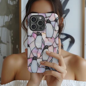 以下が含まれることがあります： 黒、白、グレーのペンギンのパターンが特徴のスマートフォンケース。ピンクと白の背景に配置されています。ケースは光沢仕上げで、スマートフォン向けに設計されています。