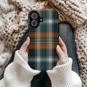 Pode incluir: Uma capa de smartphone com um padrão xadrez em tons de verde, castanho e branco. A capa tem um recorte para a câmara e é segurada por uma pessoa que usa um suéter branco. O design xadrez é um padrão clássico.
