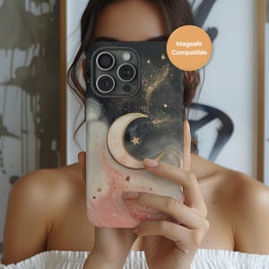 Puede incluir: Una funda de teléfono negra y dorada con un diseño celestial que presenta una luna creciente y estrellas. La funda tiene un patrón de mármol rosa y blanco en la parte inferior. El texto "Magsafe Compatible" es visible en la parte superior derecha.