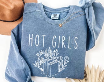 May include: A light blue sweatshirt with the text "HOT GIRLS READ" in white. The text is surrounded by a floral design with a stack of books in the center.