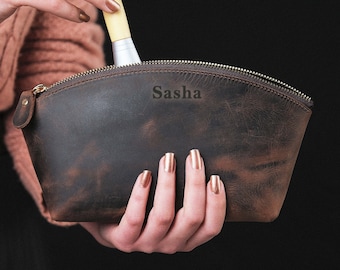 May include: A brown leather makeup bag with a zipper closure and the name "Sasha" embossed on the front.