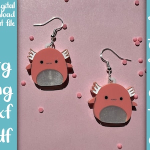 May include: A pair of pink axolotl earrings with silver glitter accents and silver earring hooks. The earrings are on a pink background with pink polka dots.